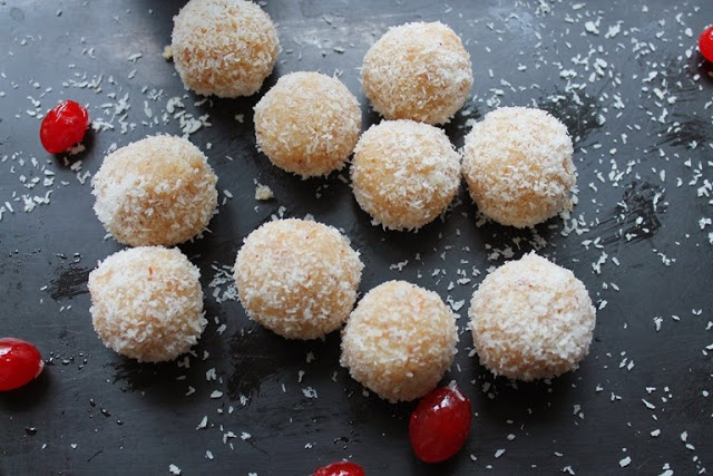 coconut ladoo displayed on a black serving dish scattered with desiccated coconut and red cherries