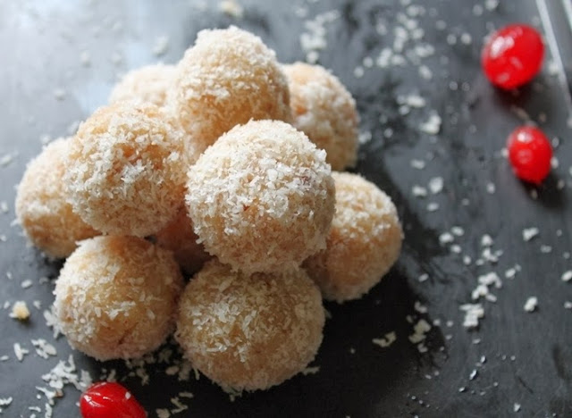 coconut ladoo stacked on a black serving dish scattered with desiccated coconut and red cherries