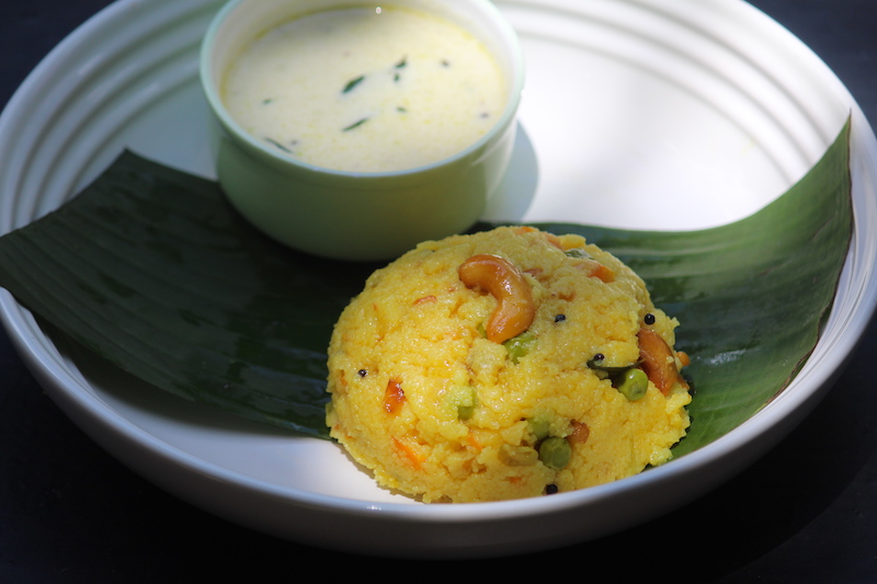 rava kichadi served with coconut chutney over a strip of banana leaf on a white plate