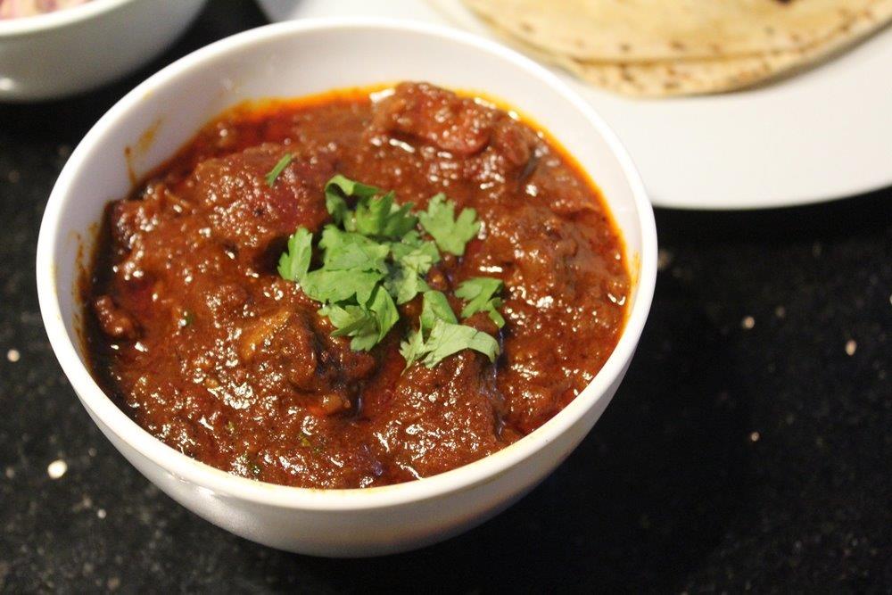 lamb vindaloo served with roti in a white bowl with coriander leaves for garnishing