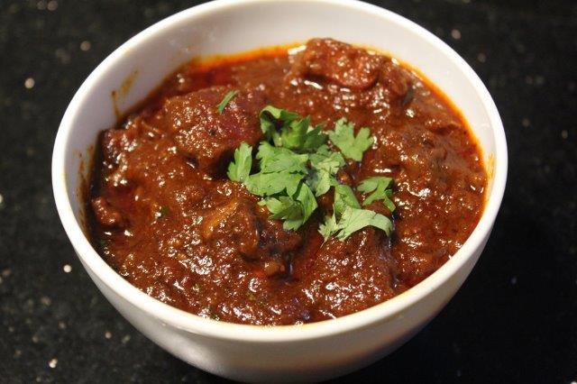 lamb vindaloo served with roti in a white bowl with coriander leaves for garnishing