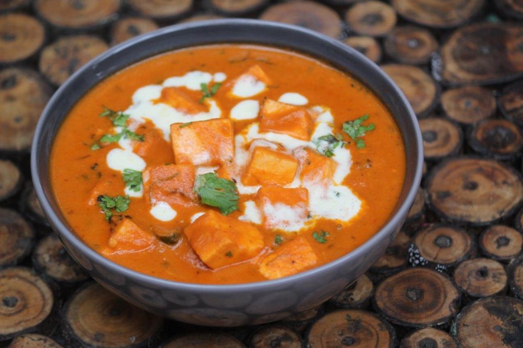 paneer butter masala served in a grey bowl with cream drizzled on top and garnished with coriander leaves