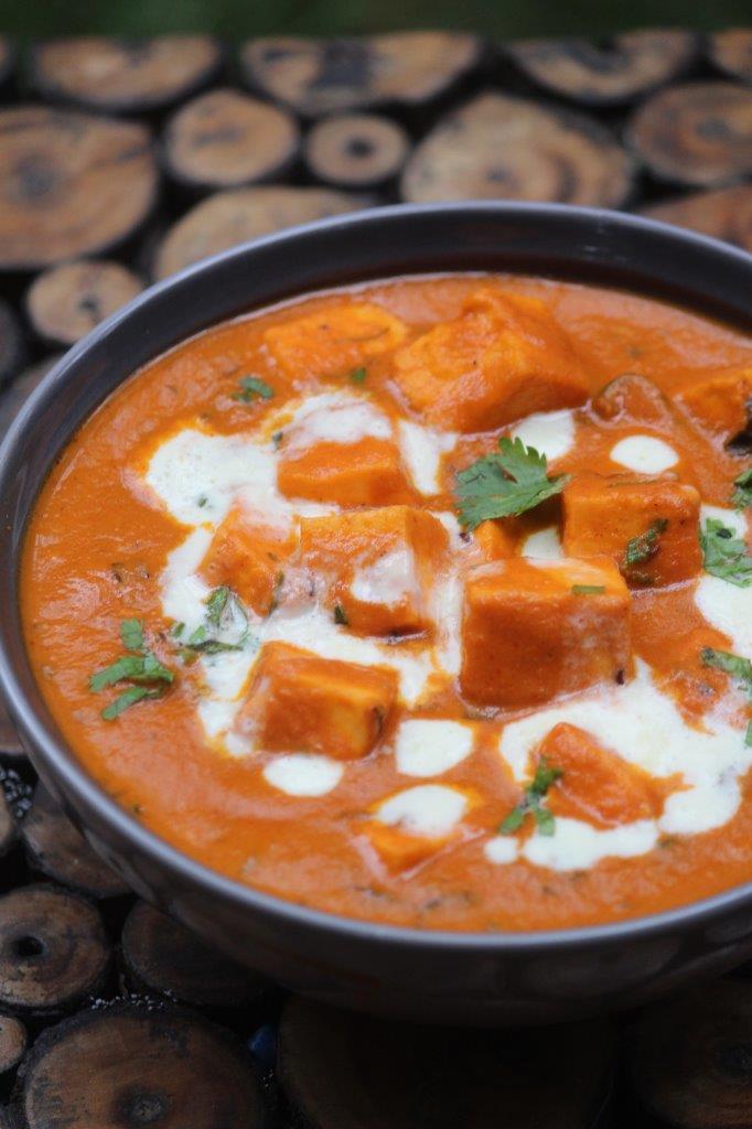 paneer butter masala served in a grey bowl with cream drizzled on top and garnished with coriander leaves