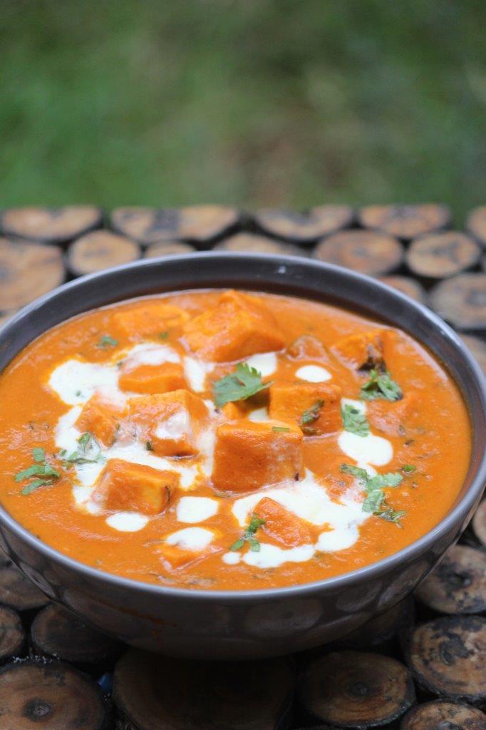 paneer butter masala served in a grey bowl with cream drizzled on top and garnished with coriander leaves