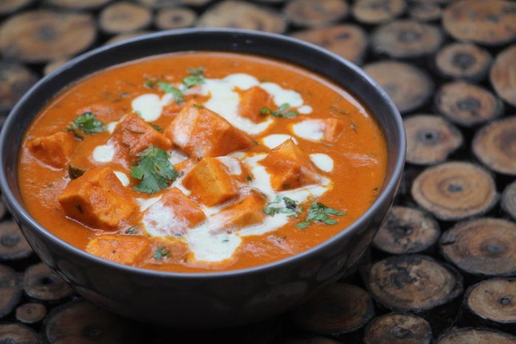 side angle of paneer butter masala in a grey bowl garnished with cream and coriander leaves