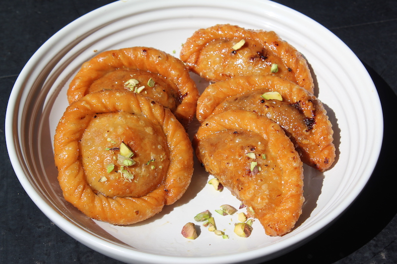 Suryakala Chandrakala Sweet served in a white plate topped with chopped nuts