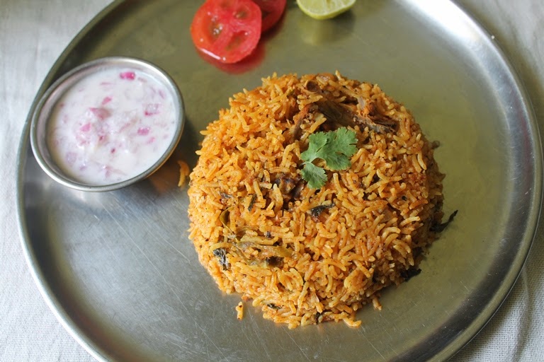 chicken biryani served with onion raita, sliced tomatoes and lemon wedges