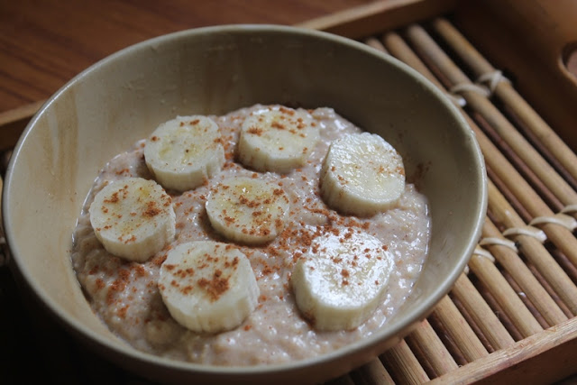 cinnamon oatmeal porridge served in a grey colour bowl with sliced bananas on top and hit with a dash of cinnamon powder
