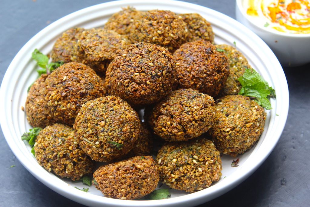 a plate filled with crispy falafels served with tahini sauce on the side