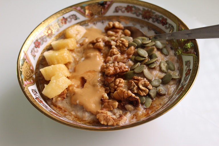 creamy oats porridge topped with sliced bananas, almond butter, walnuts, pumpkin seeds and drizzled with maple syrup