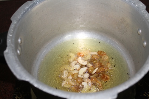 heat oil and ghee in a pressure cooker. Add cashews and raisins and fry till golden brown