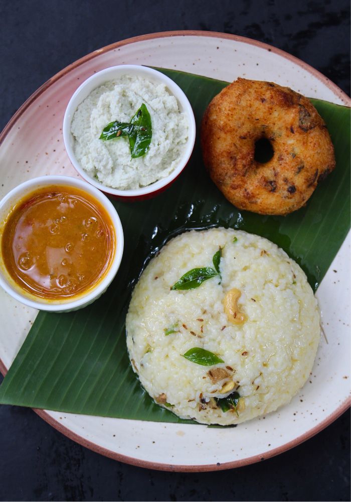top shot of ven pongal served with coconut chutney, sambar and medu vada in a banana leaf
