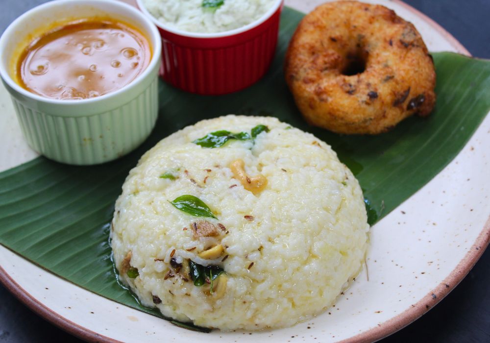 ven pongal served with coconut chutney, sambar and medu vada in a banana leaf