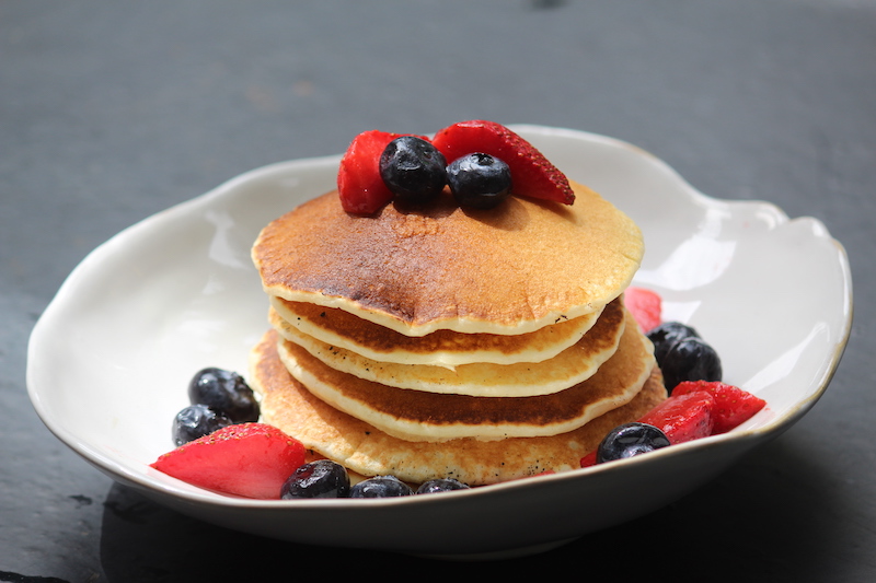 stack of pancakes served with berries on a white plate