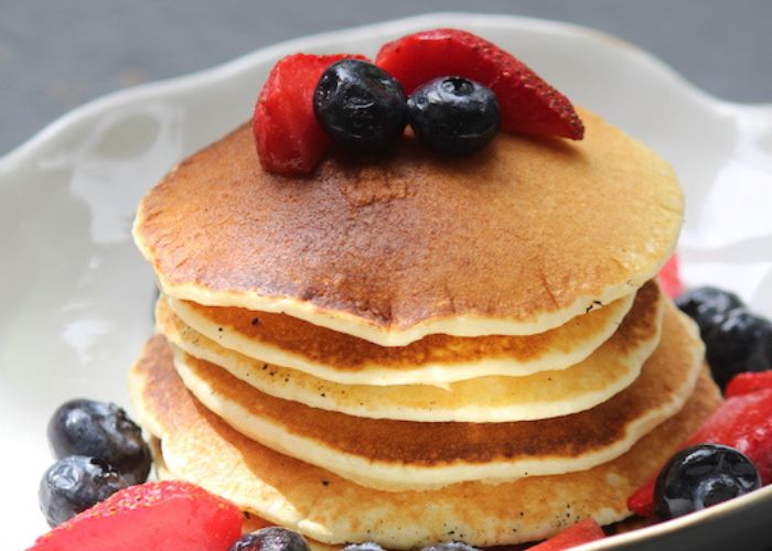 stack of pancakes served with berries on a white plate