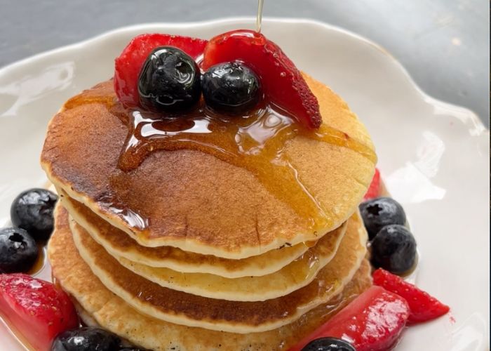 stack of pancakes served with berries  drizzled with maple syrup on a white plate