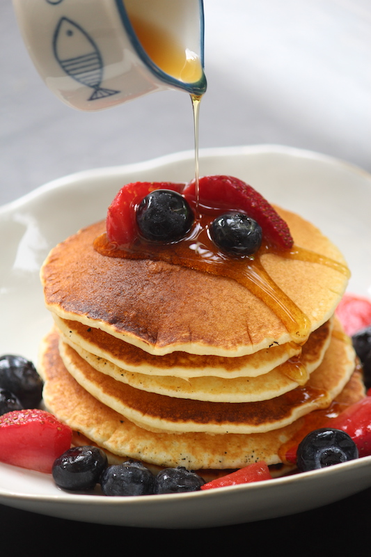 stack of pancakes served with berries drizzled with maple syrup on a white plate