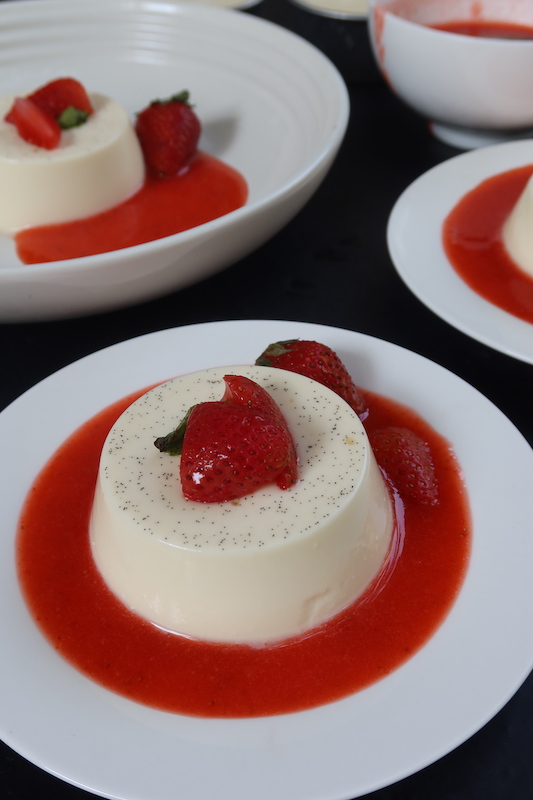 close look of vanilla bean specked panna cotta served with strawberry coulis and fresh berries