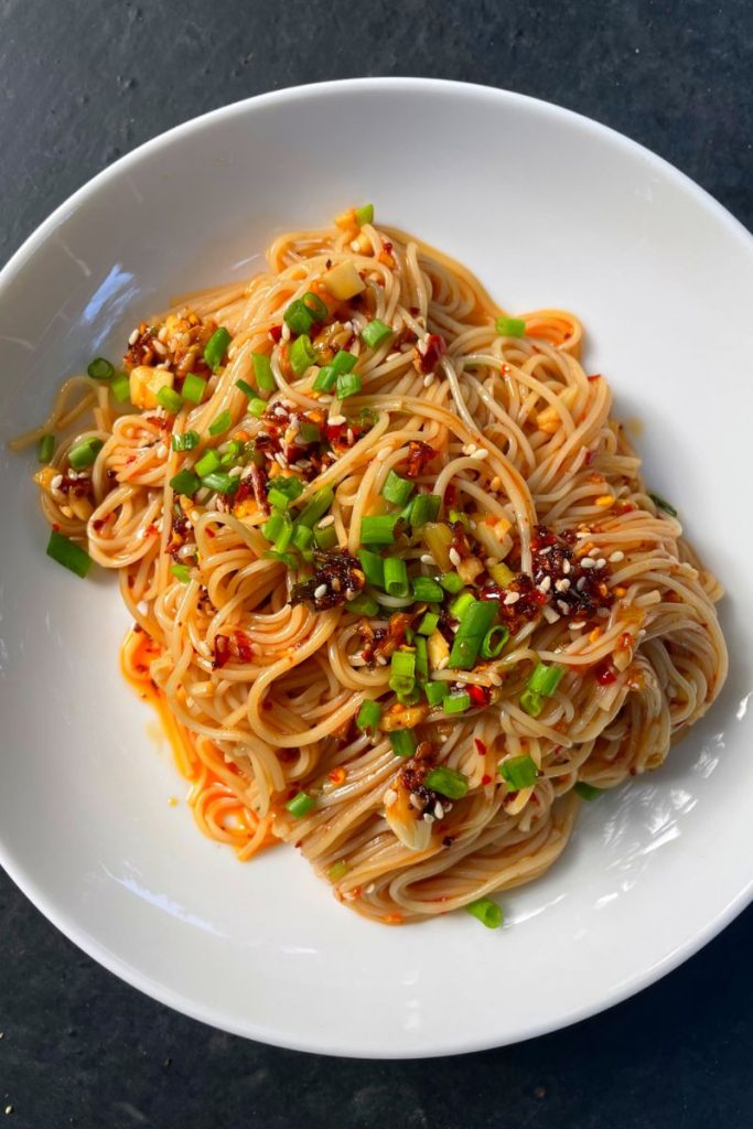 close look of chilli oil noodles served with chilli crispy, spring onions and sesame seeds