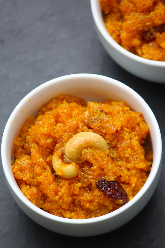 close shot of carrot halwa served in a white bowl with fried cashews on top for garnishing
