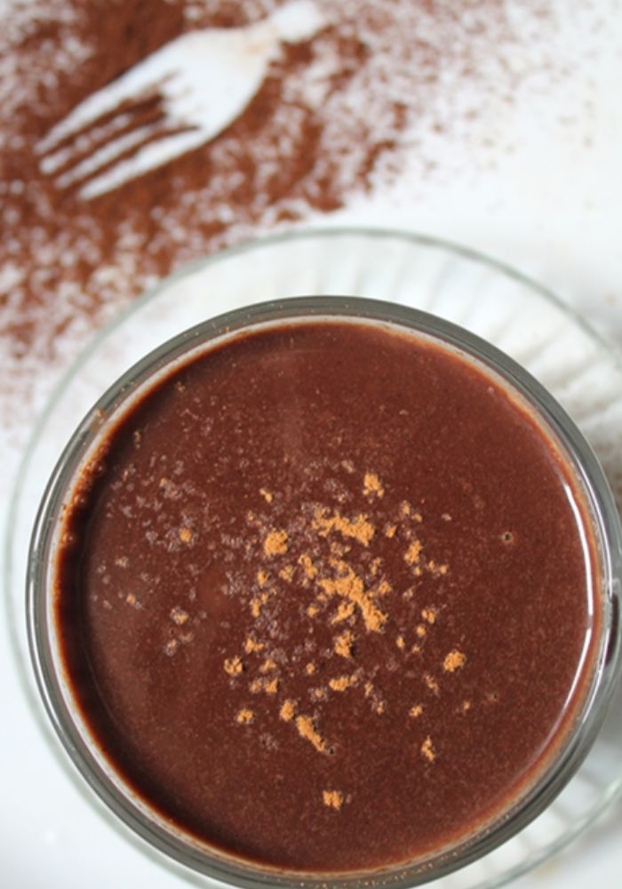 top angle of rich hot chocolate served in a glass cup with a sprinkle of cocoa powder on top 