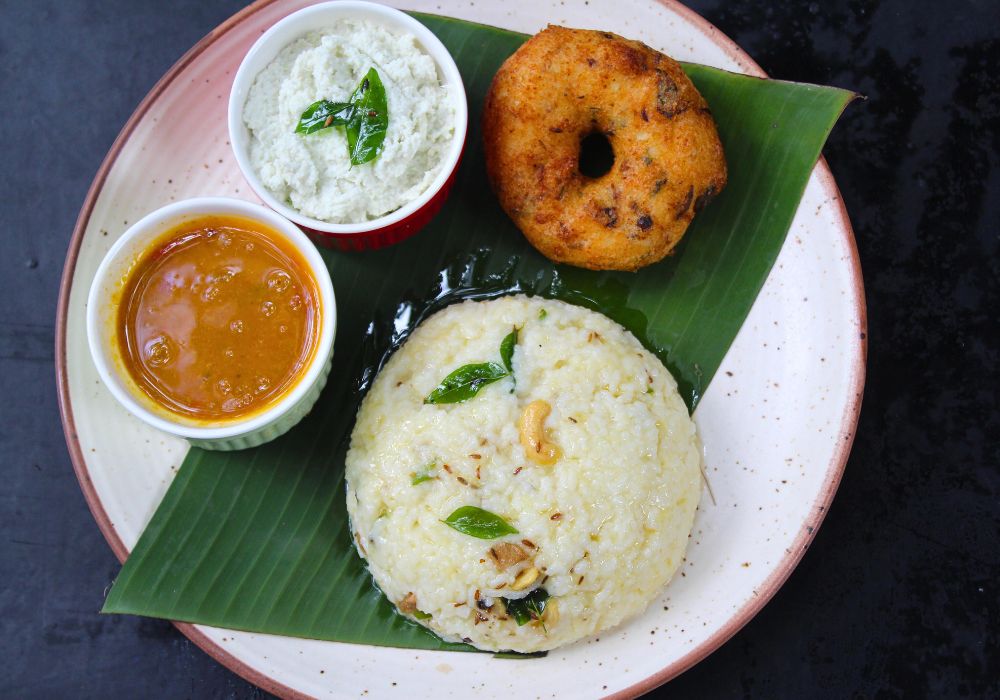 ven pongal served with coconut chutney, sambar and medu vada in a banana leaf